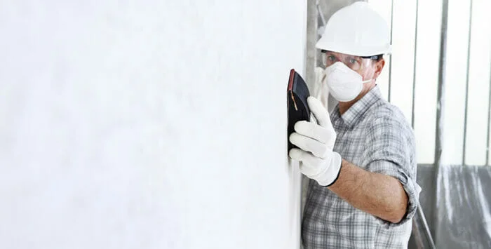 construction worker wearing a mask whilst sanding drywall